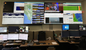 Real-time monitoring through displays showing pertinent information, with AX’s FireScout SaaS AI front and center, actively detecting a smoke plume in the distance.